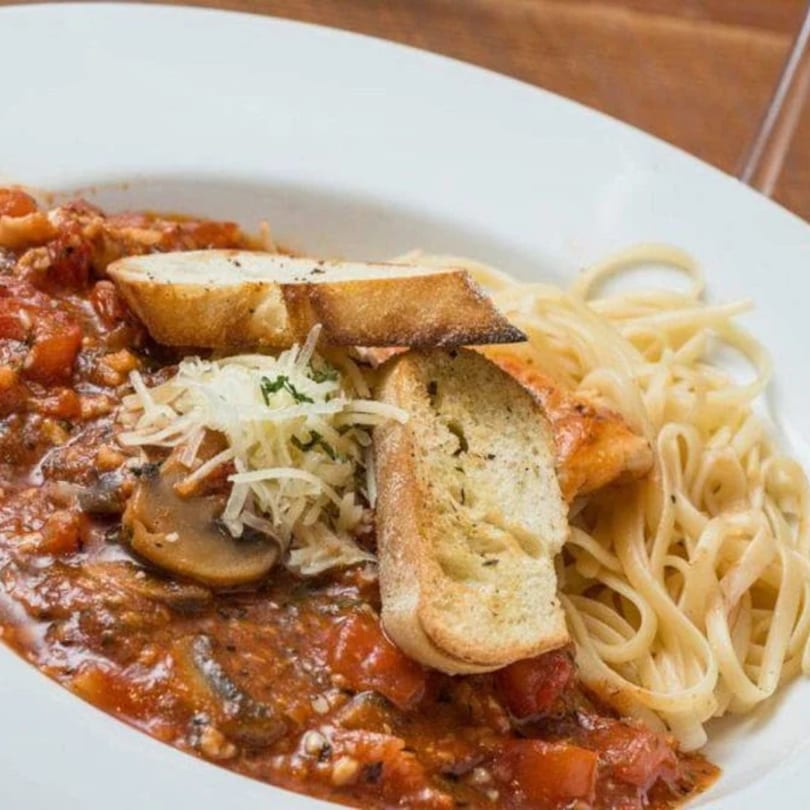 A white bowl filled with spaghetti, red sauce, mushrooms, shredded cheese, and two slices of bread.