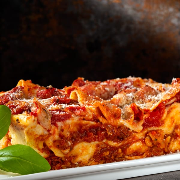 Close-up of a cheesy lasagna slice with rich red sauce, ground meat, and fresh basil leaves.