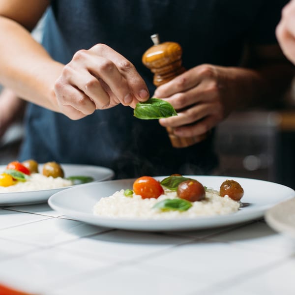 Chef garnishing creamy risotto with fresh basil leaves, cherry tomatoes, and meatballs.