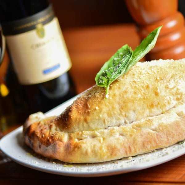 Golden-brown calzone topped with fresh basil and parmesan, with a wine bottle in the background.