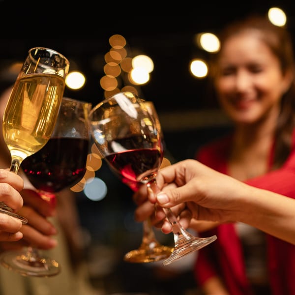 Three people clinking glasses of red wine and champagne, with a blurred smiling woman in red in the background.