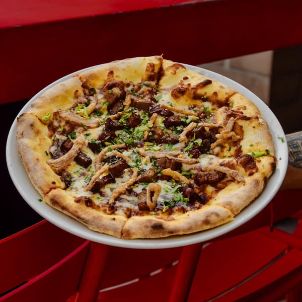 A freshly baked pizza with meat, cheese, and herbs on a white plate, held over a red surface.