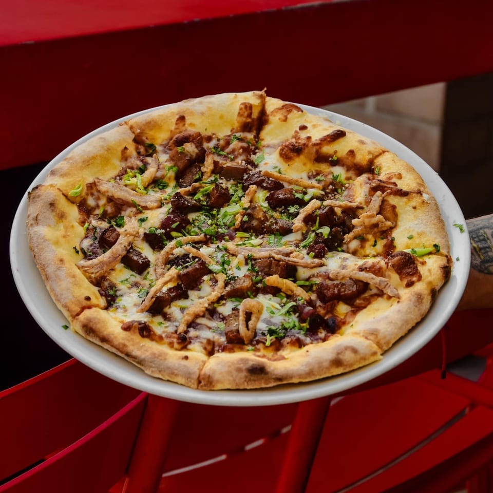 A freshly baked pizza with meat, cheese, and herbs on a white plate, held over a red surface.