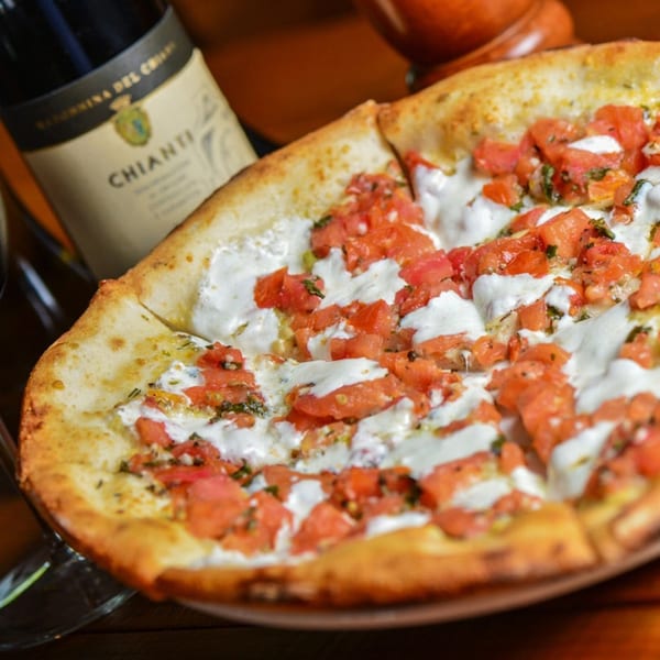 A delicious bruschetta pizza with fresh tomatoes, mozzarella, and basil, next to a bottle of Chianti.
