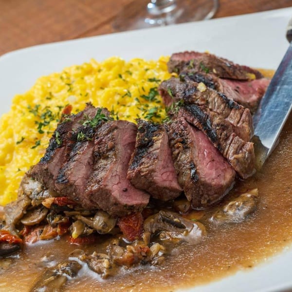 Sliced steak with gravy, mushrooms, sun-dried tomatoes, and yellow rice on a white plate.