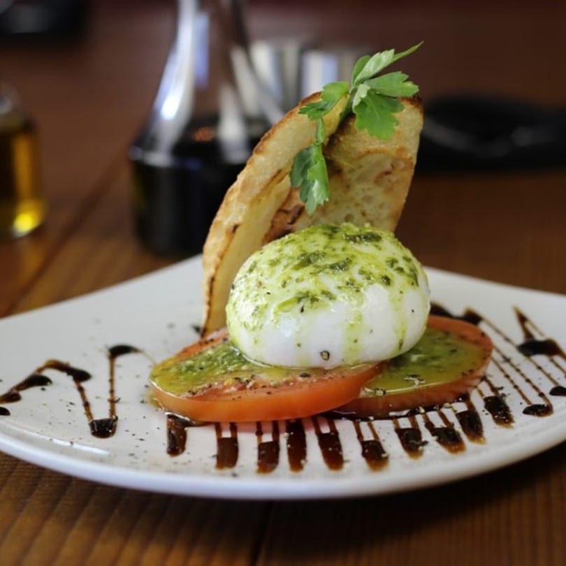 Caprese salad with fresh mozzarella, sliced tomatoes, pesto, balsamic glaze, and toasted bread.