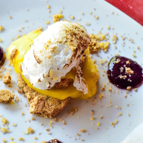 Lemon meringue dessert with graham cracker crust and berry sauce on a white plate.