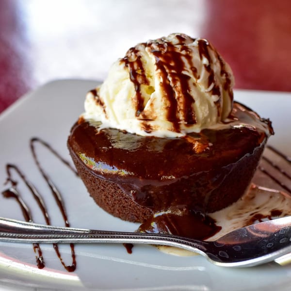 Warm chocolate lava cake topped with vanilla ice cream and chocolate syrup on a white plate with a spoon.