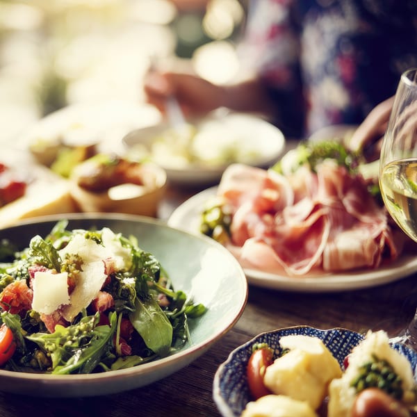 Close-up of a fresh salad with parmesan and prosciutto, with a glass of white wine.